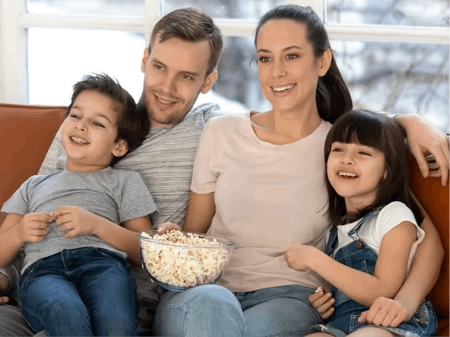 Family smiling and watching television with bowl of popcorn