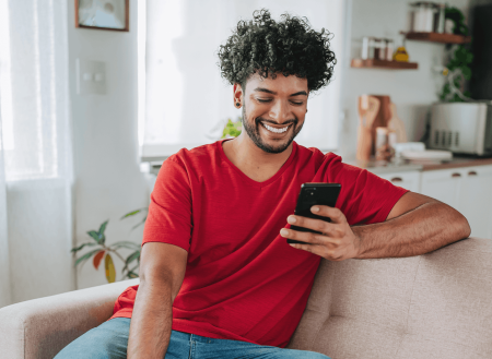 Man in red shirt sitting on couch and using phone