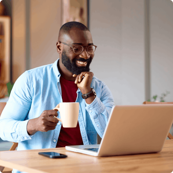Man sitting at desk using laptop and drinking coffee