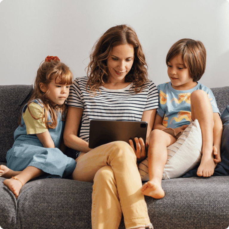 Mother using tablet on couch with kids sitting beside her